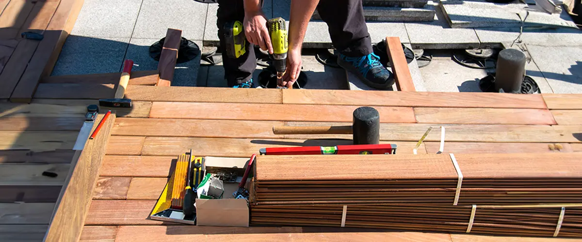 Construction worker using a drill for deck installation in Gladwine, with various tools and materials on the work surface.