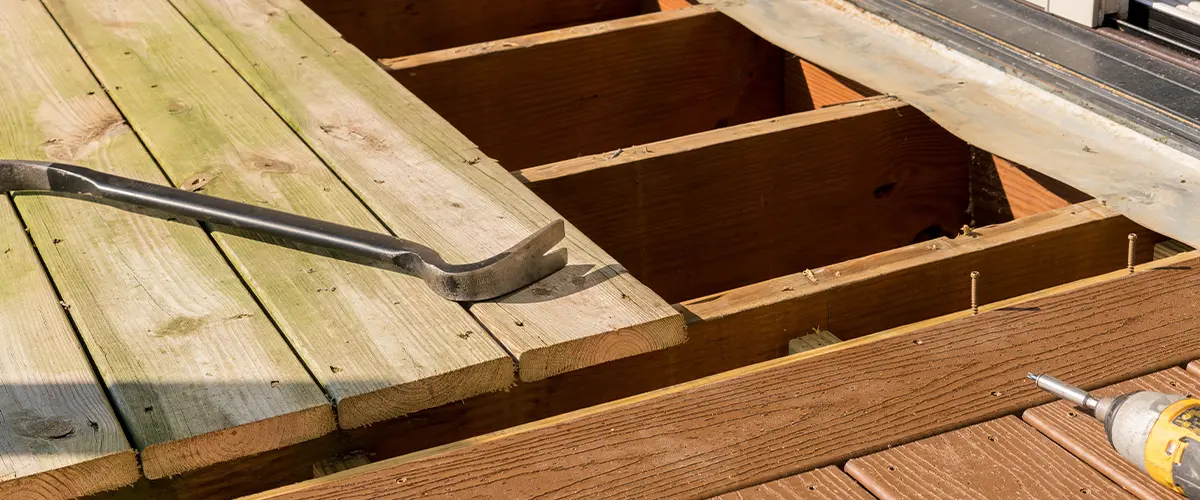 Replacing wooden deck boards in deck repair project in Lansdale, with composite decking, showing old green wooden planks removed, new brown composite boards, and tools like a pry bar and drill.