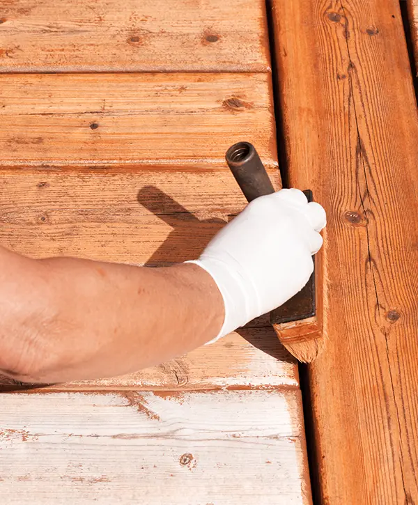 Hand with a brush applying stain to weathered wooden boards