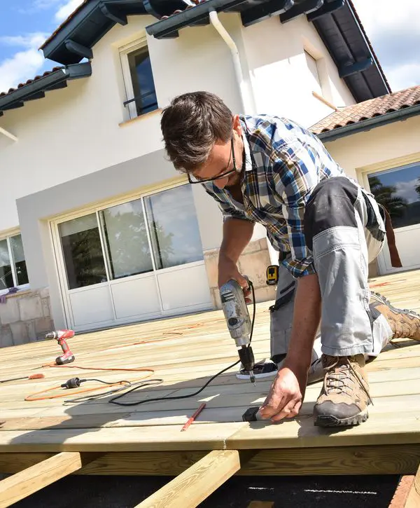 Man drilling screws into wooden deck boards on a house deck under construction