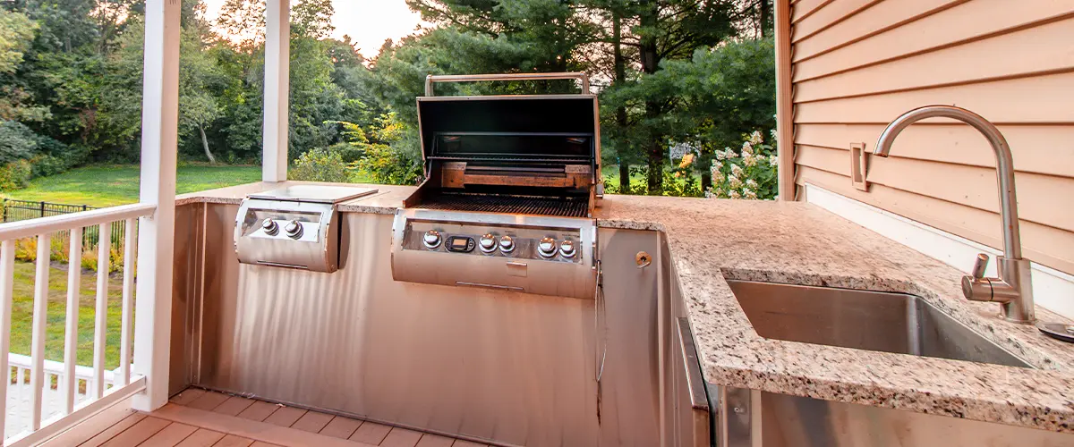 Outdoor kitchen on a deck with a stainless steel grill, sink, and granite countertops under a covered patio