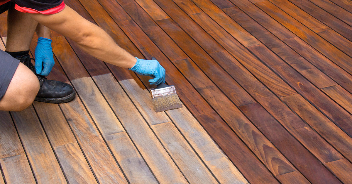 Person applying stain to faded wooden deck boards with a brush