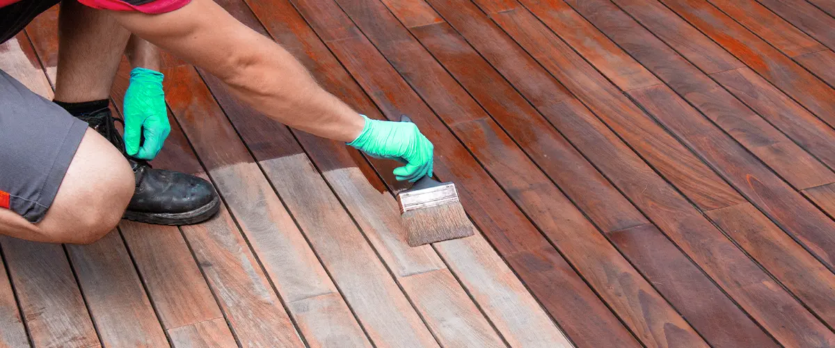 Person applying stain to faded wooden deck boards with a brush