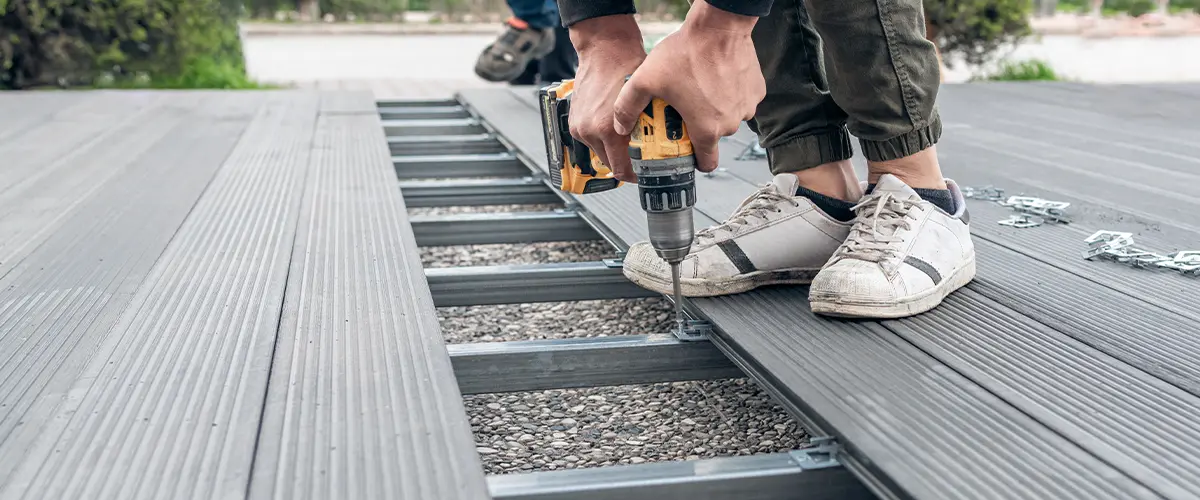 Contractor using a power drill to repair composite decking on a metal frame during outdoor deck repair