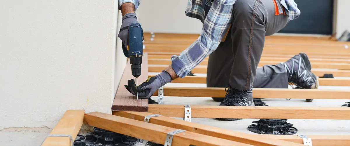 Deck builder drilling wooden planks for outdoor deck construction.