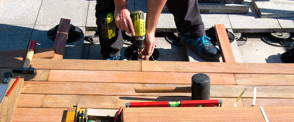 Carpenter installing wooden deck boards with power drill, construction tools in view - professional decking installation process.