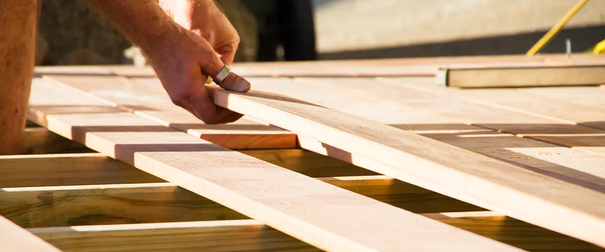 Close-up of a carpenter installing wooden deck planks, focusing on hands aligning and securing boards during deck construction.