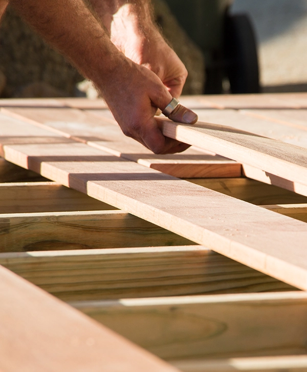 A worker constructing a new wooden deck, measuring and cutting planks by top Deck Builder in Gladwyne, PA