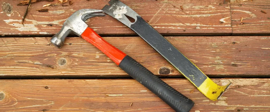 Hammer and pry bar on a worn wooden deck, symbolizing deck repair, renovation, and home improvement projects.