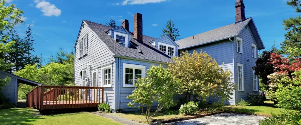 Charming gray cottage-style home with backyard deck and lush landscaping under a bright blue sky