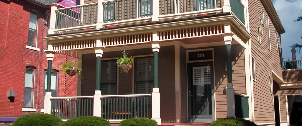 Classic two-story American home with brown siding, upper balcony, and manicured front yard landscaping