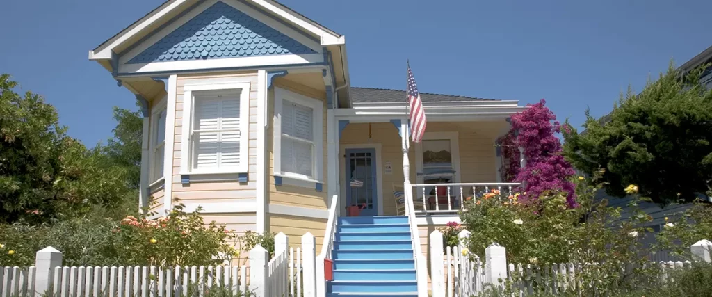 Colorful Victorian home with blue stairs, white picket fence, and vibrant garden flowers in front yard