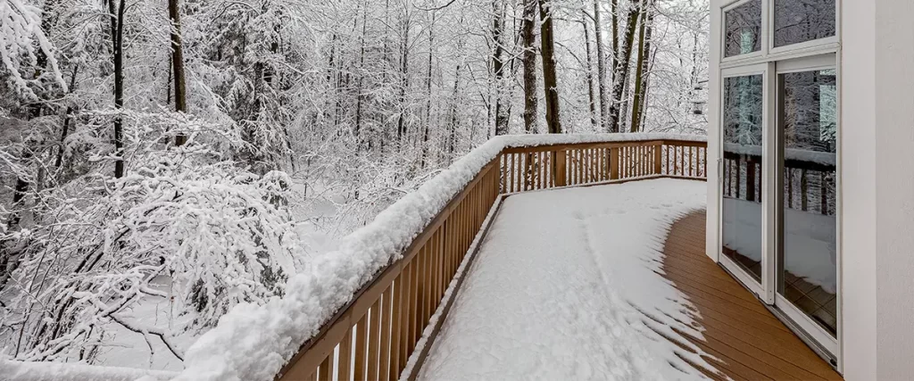 Modern home deck with fresh snowfall in a wooded backyard during winter season