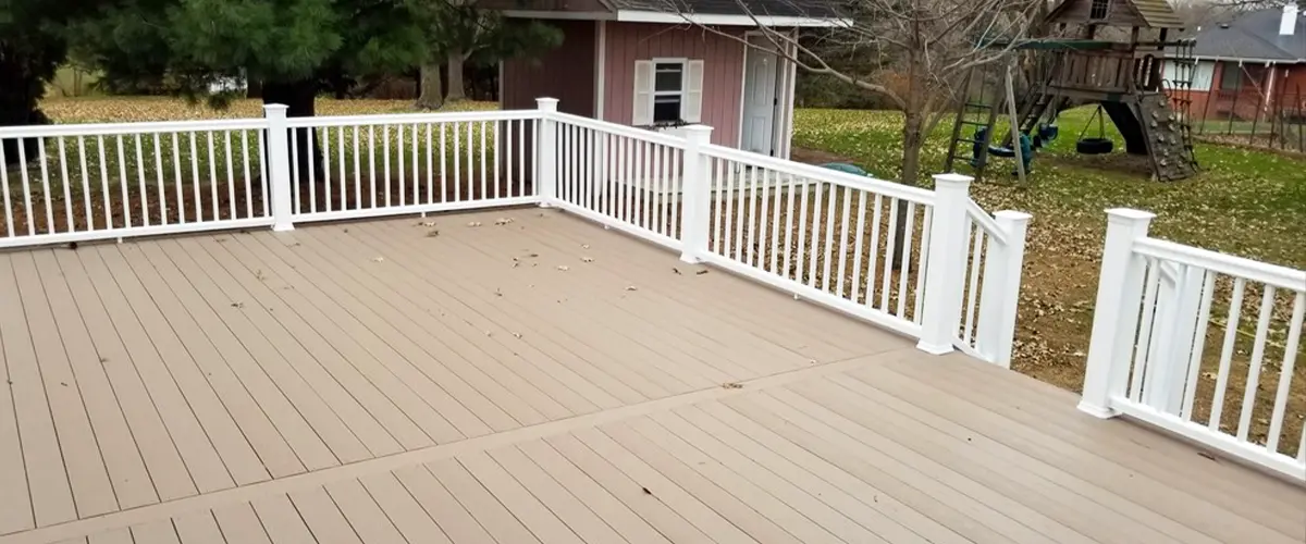 Spacious composite backyard deck with white vinyl railing overlooking lawn and play area with swing set.