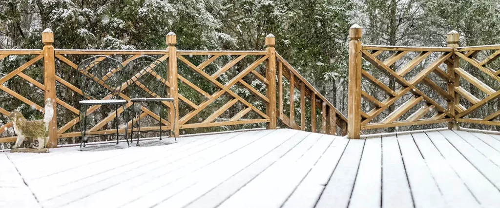 Wood deck covered in snow with rustic railing and forest backdrop during winter snowfall