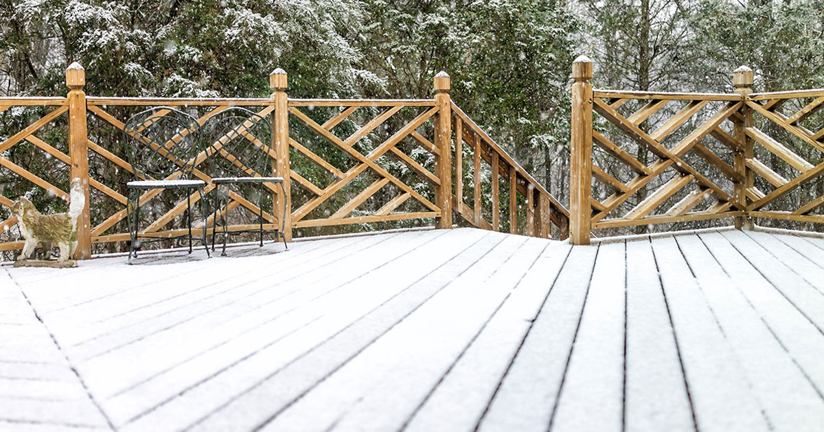 Wood deck covered in snow with rustic railing and forest backdrop during winter snowfall