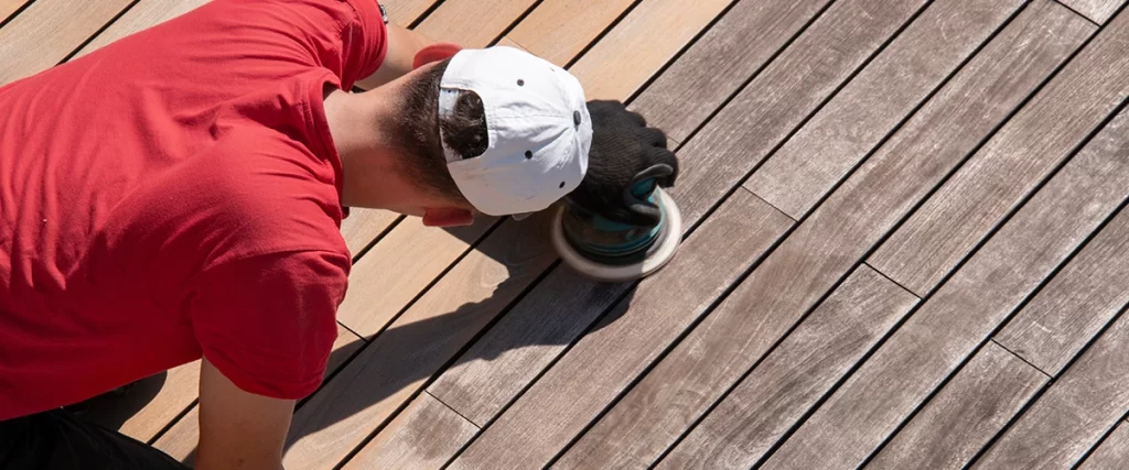 Person using orbital sander to refinish weathered wood decking boards before applying new stain