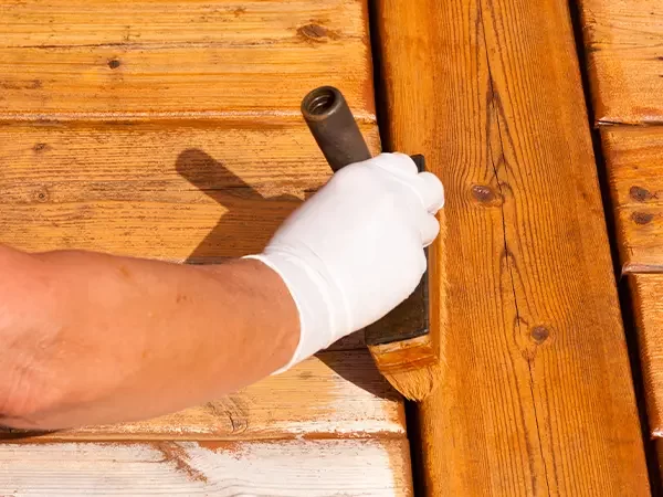 Hand with a brush applying stain to weathered wooden boards